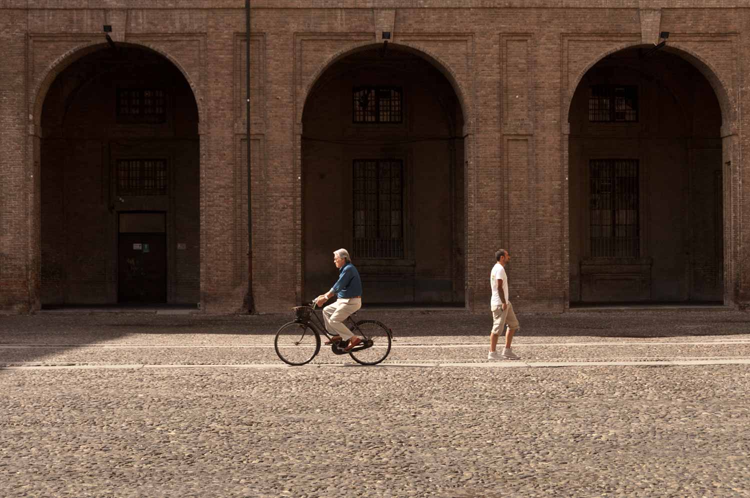 In the internal courtyard, a cyclist passes a pedestrian headed for Parco Ducale.
